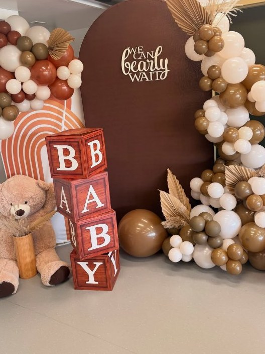 Baby shower by Rose & Novah: a chocolate brown arch backdrop reading We Can Bearly Wait, framed by brown, cream and terracotta balloon garlands with dried palms, BABY blocks and a teddy bear