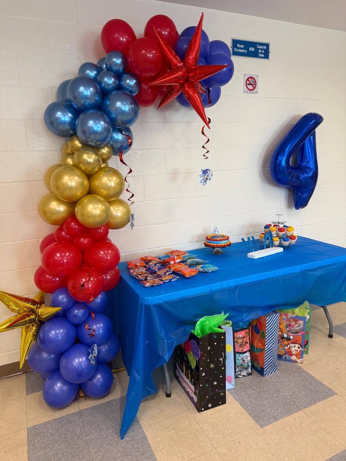 Fourth birthday setup with a red, blue and gold balloon garland, star balloons and dessert table